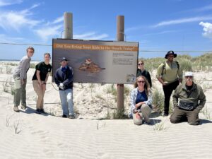 Beach stewards in front of a sign on the beach.