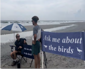 Beach stewards on the bach next to Ask Me About the Birds sign. USFWS photo